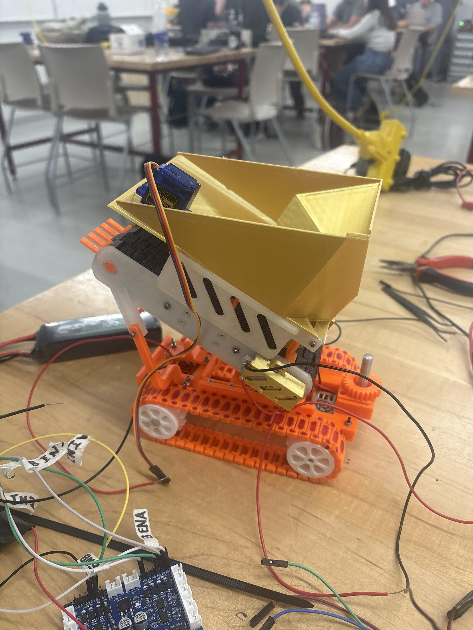 Robot with tilted collection hopper on a workbench, showing internal wiring and servo
